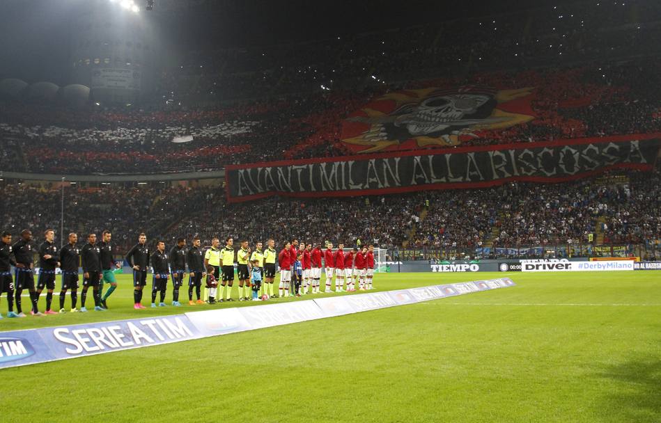 Squadre pronte a metà campo: sullo sfondo la coreografia dei tifosi del Milan.